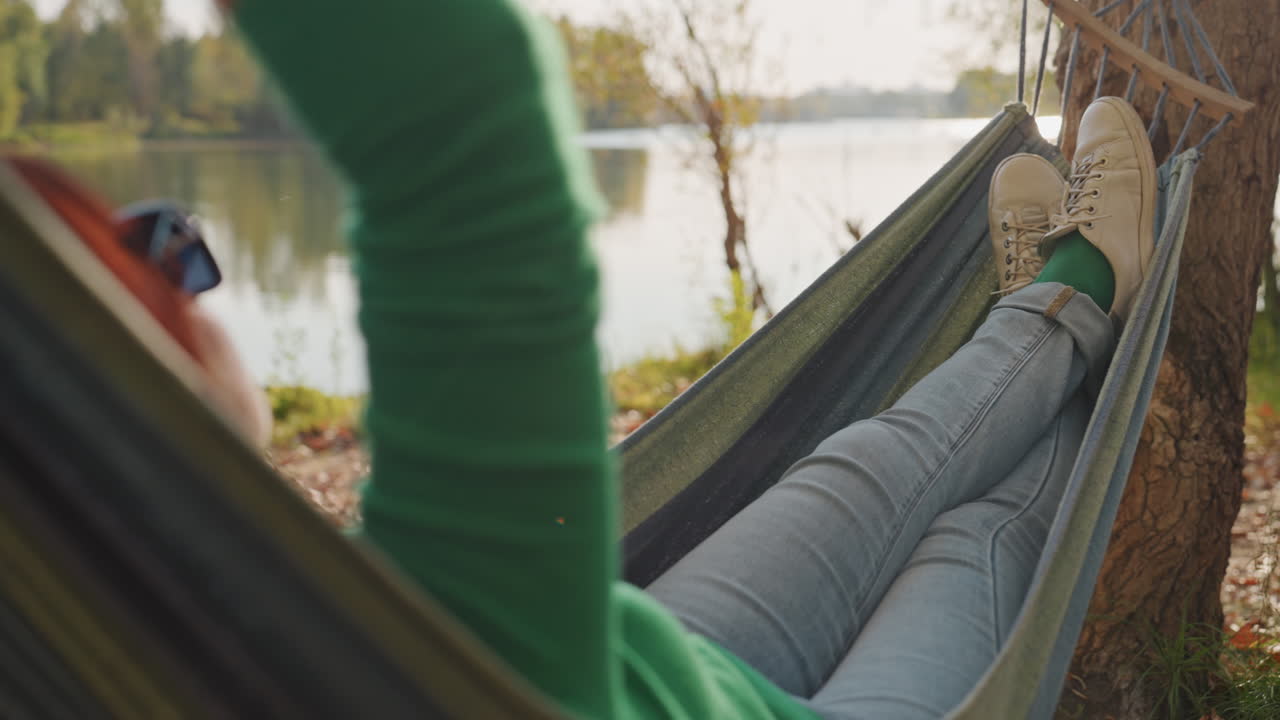 Relaxing lakeside retreat. Woman resting by tranquil water. Serene scene of woman in hammock enjoying nature. Peaceful moment captured of woman recharging beside lake during outdoors leisure
