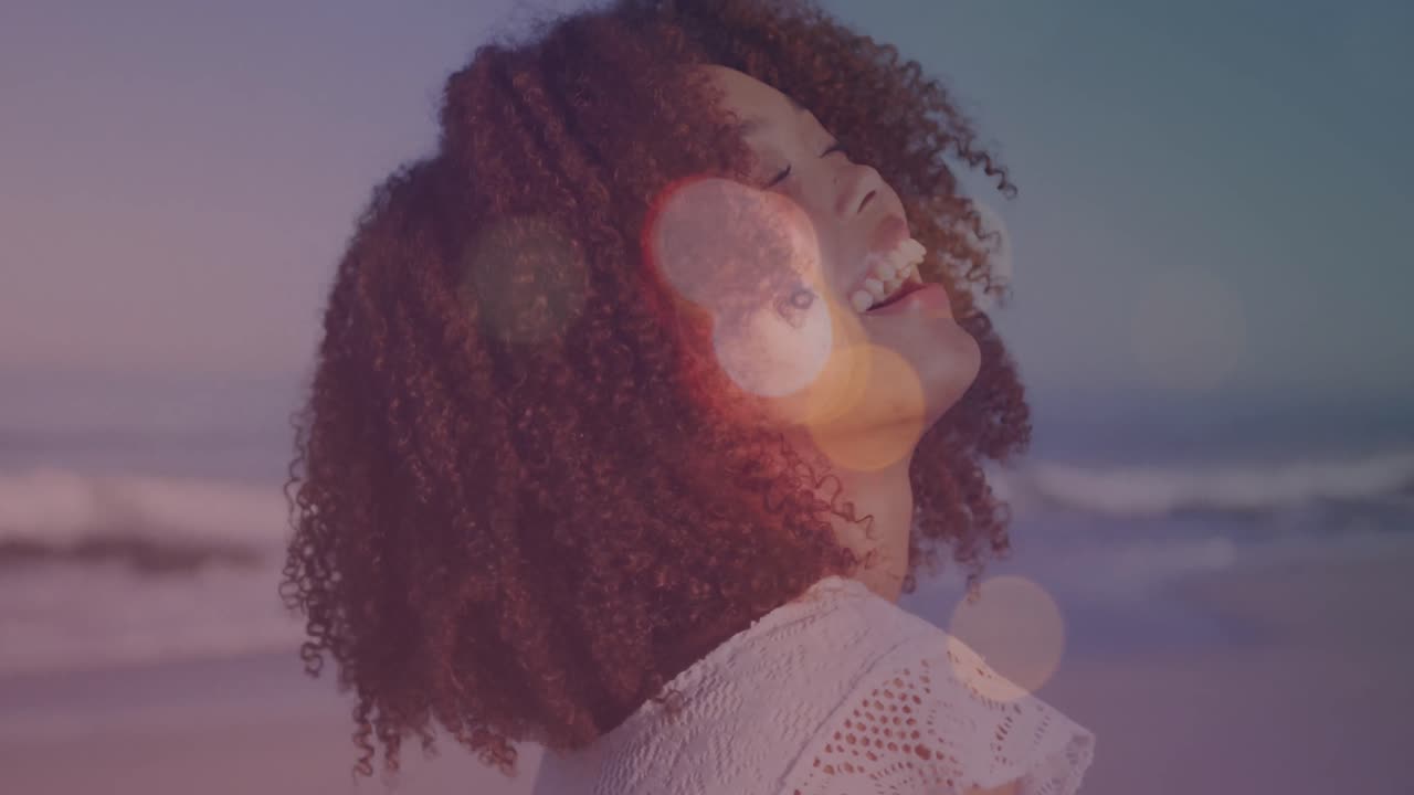Animation of lens flares over portrait of biracial young woman with afro hair laughing at beach