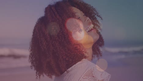 Animation-of-lens-flares-over-portrait-of-biracial-young-woman-with-afro-hair-laughing-at-beach