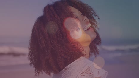 animación de llamaradas de lente sobre el retrato de una joven biracial con cabello afro riendo en la playa.
