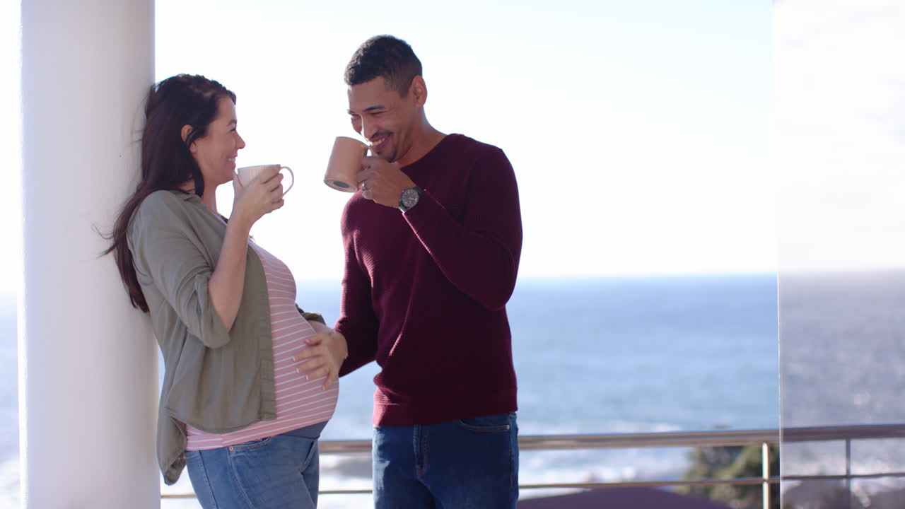Pregnant couple smiling and drinking coffee while looking at smartphone