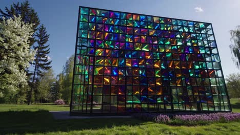 sunlight streaming through multicolored glass panels, transforming park landscape with vibrant architectural design, creating mesmerizing prismatic reflections across serene green surroundings