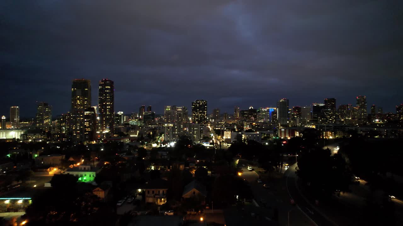 Dron volando hacia el centro de San Diego con las luces de la ciudad brillando en el horizonte por la noche