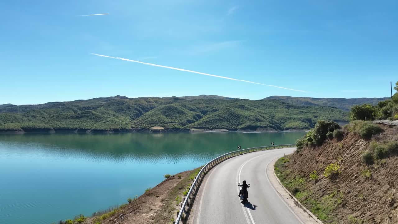 青い湖のある美しい景色を見下ろす人気のない道を一人で走るバイカー。
