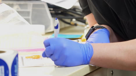 nurse prepares to administer the covid 19 shot or corona virus vaccine injection by gathering clean syringe needles and filling out vaccine card in medical doctor’s office with no faces