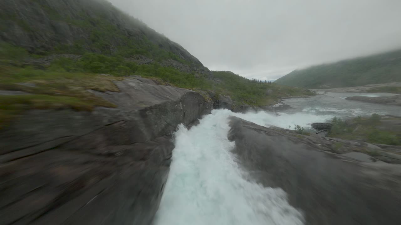 노르웨이의 내리막길에서 추락하는 물줄기 위의 다리 아래로 비행하는 드론 조종사