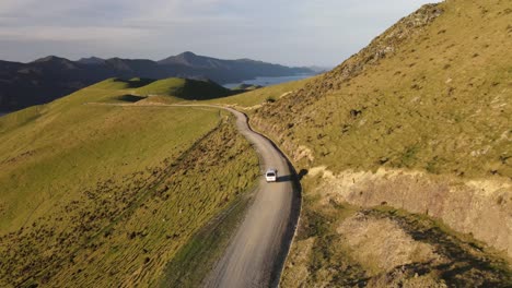 Seguimiento-Aéreo-De-Un-Coche-Que-Viaja-Por-Una-Carretera-De-Montaña-Durante-La-Puesta-De-Sol-En-El-Paso-Francés-Estrecho-En-Nueva-Zelanda