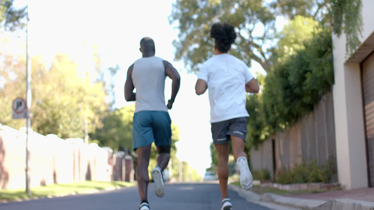 Running outdoors, two multiracial male friends exercising on suburban street, enjoying workout