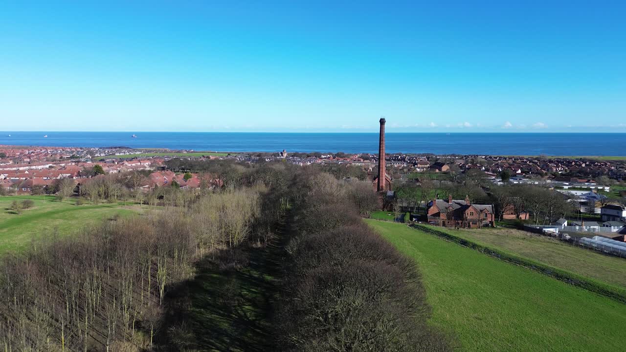 Drone stiger op over Ryhope Engines Museum og afslører en høj murstensskorsten, skov og grønne marker, Sunderlands hustage og Nordsøens horisont under klar blå himmel.