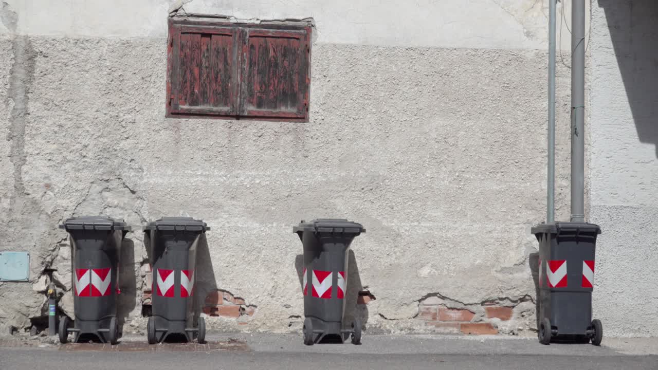 Four Grey Wheeled Bins Against a Weathered Wall