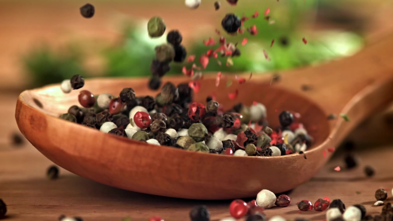Mixed Peppercorns Falling into a Wooden Spoon in Slow Motion
