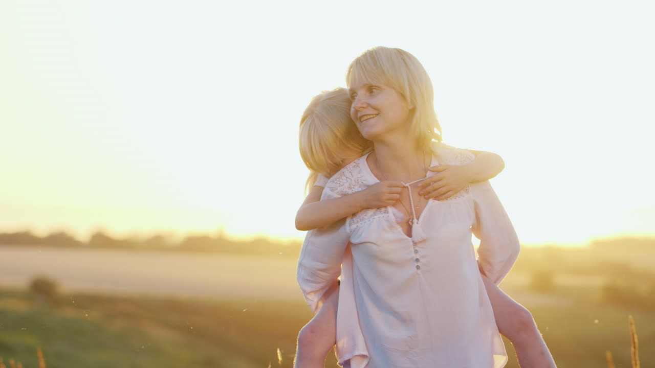 멋진 젊은 엄마가 예쁜 딸과 함께 잔디밭에서 여름 일몰과 자연을 즐기며 논다