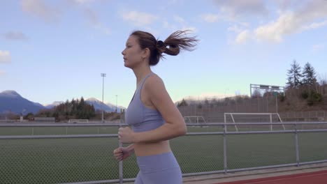 mujer asiática de raza mixta trotando en la pista, siguiendo el perfil de cámara lenta