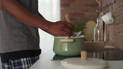 Hombre-Africano-Hirviendo-Agua-En-Una-Olla-Parada-En-La-Cocina,-Filmada-En-Cámara-Lenta