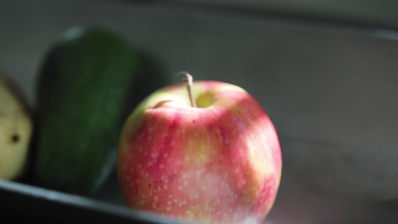 Pan up revealing an apple and an avo in a silver fruit bowl