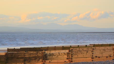 distant clouds moving across mountain peaks with foreground sea and breakwaters glowing in evening sun