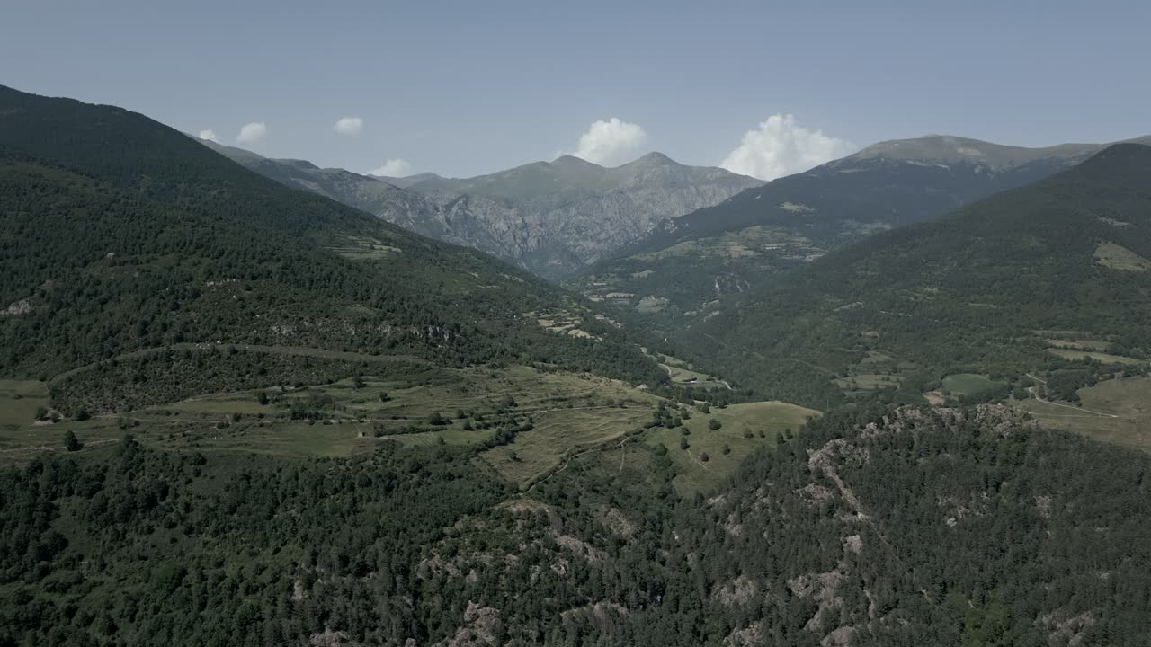 Breathtaking aerial perspective reveals the lush green valley nestled within the majestic pyrenees mountains of catalonia, under a serene blue sky dotted with small white clouds