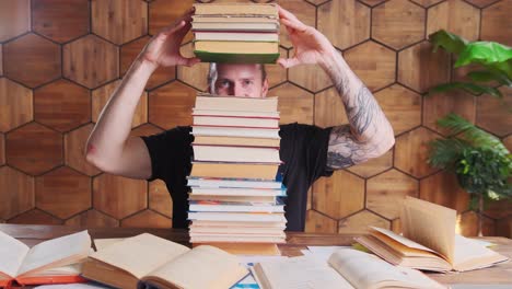 joven caucásico se divierten escondiendo los ojos detrás de la montaña de libros se sienta en la mesa