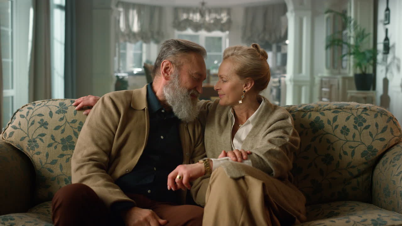 pareja de ancianos sonrientes hablando en el sofá de la sala de estar. personas mayores felices