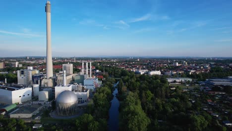 large round storage tank with a high white chimney of a large power station in the german city of braunschweig on the river oker with a clear blue sky in the background