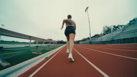 atleta de pista femenina corriendo en la pista roja en el campo de fútbol al aire libre en cámara lenta extrema, 4k 800fps corredora ojo de pez sigue por detrás