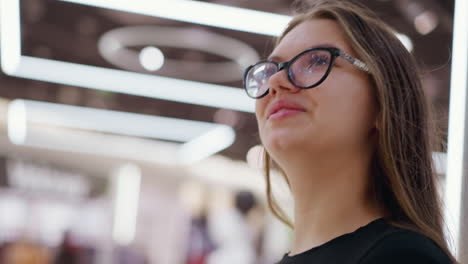 primer plano de una trabajadora remota ajustando su cabello mientras mira algo en el fondo, con una vista borrosa de la tienda, mostrando una experiencia de compras relajada o un día casual en el trabajo