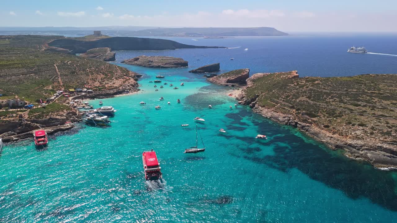 La Laguna Blu, Comino, Malta, e le vicine isole di Cominotto sono circondate da acque mediterranee turchesi e cristalline, barche e costa rocciosa in questa tranquilla vista con drone in una soleggiata giornata di primavera