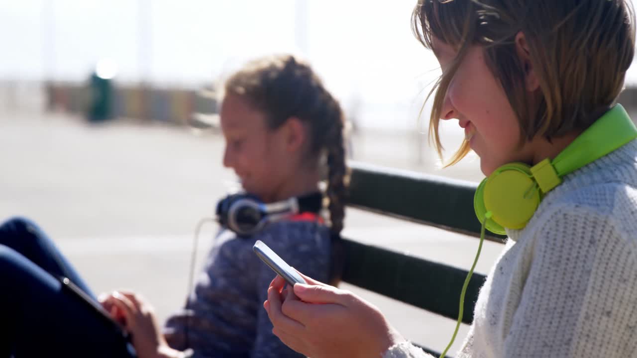 해변 4k에서 휴대 전화와 디지털 태블릿을 사용하는 형제자매