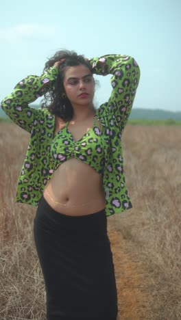young woman posing confidently in dry field wearing bold green patterned outfit