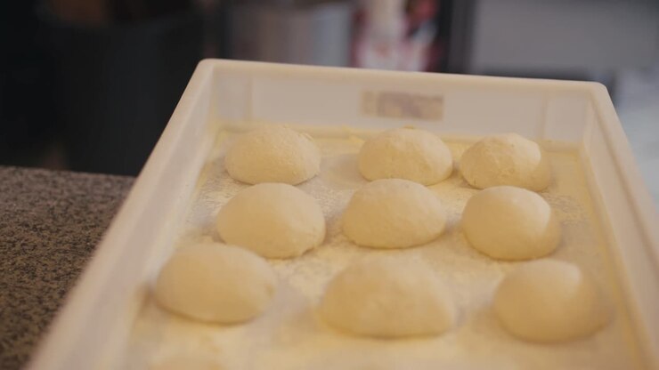 Fresh pizza dough balls on tray, ready for baking in a kebab shop kitchen, focus on foreground