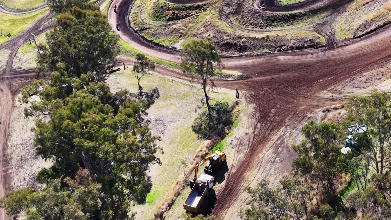 Drone captures vehicles, trees, and winding dirt track under bright daylight at outdoor recreation area
