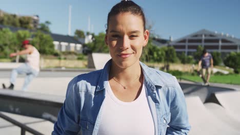 Portrait-of-smiling-caucasian-woman-on-sunny-day,-skateboarders-in-background