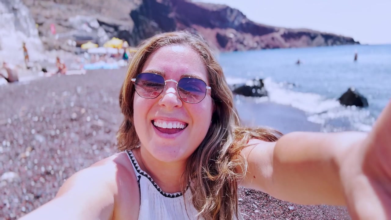 Vlogger felice che si scatta un selfie sulla spiaggia rossa a Santorini, Grecia.