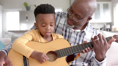 Happy-african-american-grandfather-and-grandson-playing-guitar-together-at-home,-slow-motion