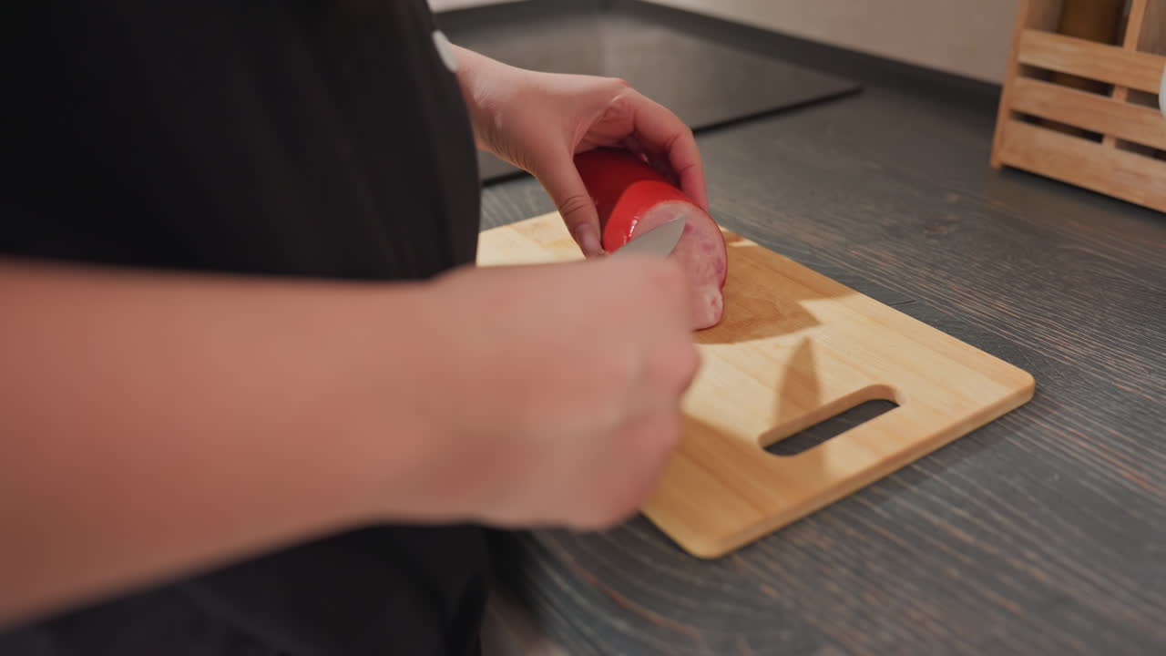 hotdog placed on wooden cutting board on kitchen counter as person opens drawer to retrieve knife and prepares to slice meat during food preparation in modern kitchen environment
