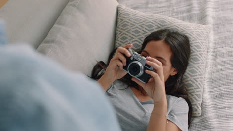 happy couple taking photos together using camera having fun relaxing at home on sofa enjoying romantic relationship playfully photographing each other