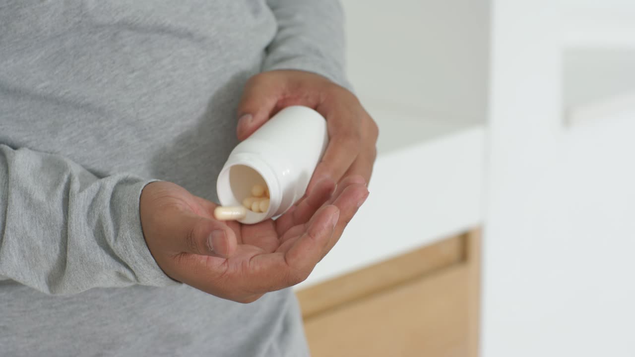 Video verticale: Uomo inclinato in camicia grigia che versa pillole nella mano al lavandino, prendendo medicine dalla bottiglia.