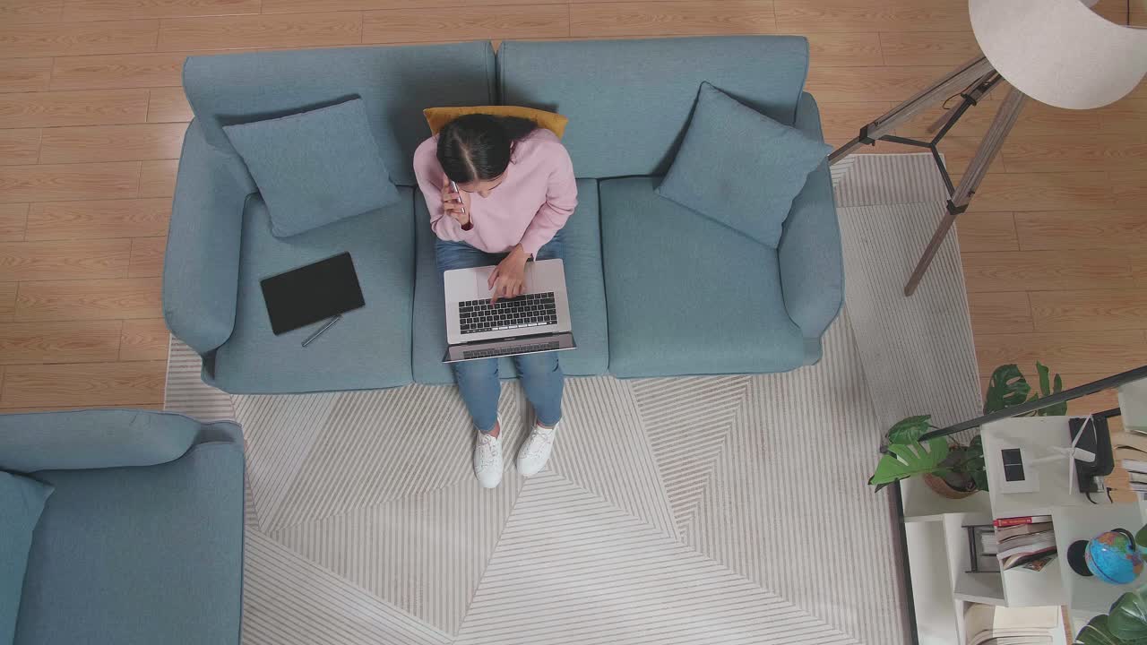vista superior de una mujer hablando en un teléfono inteligente mientras escribe en una computadora portátil en el sofá en casa