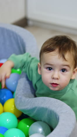 lovely kid plays at the dry pool filled with colorful toys. small child plays indoors. top view. vertical video