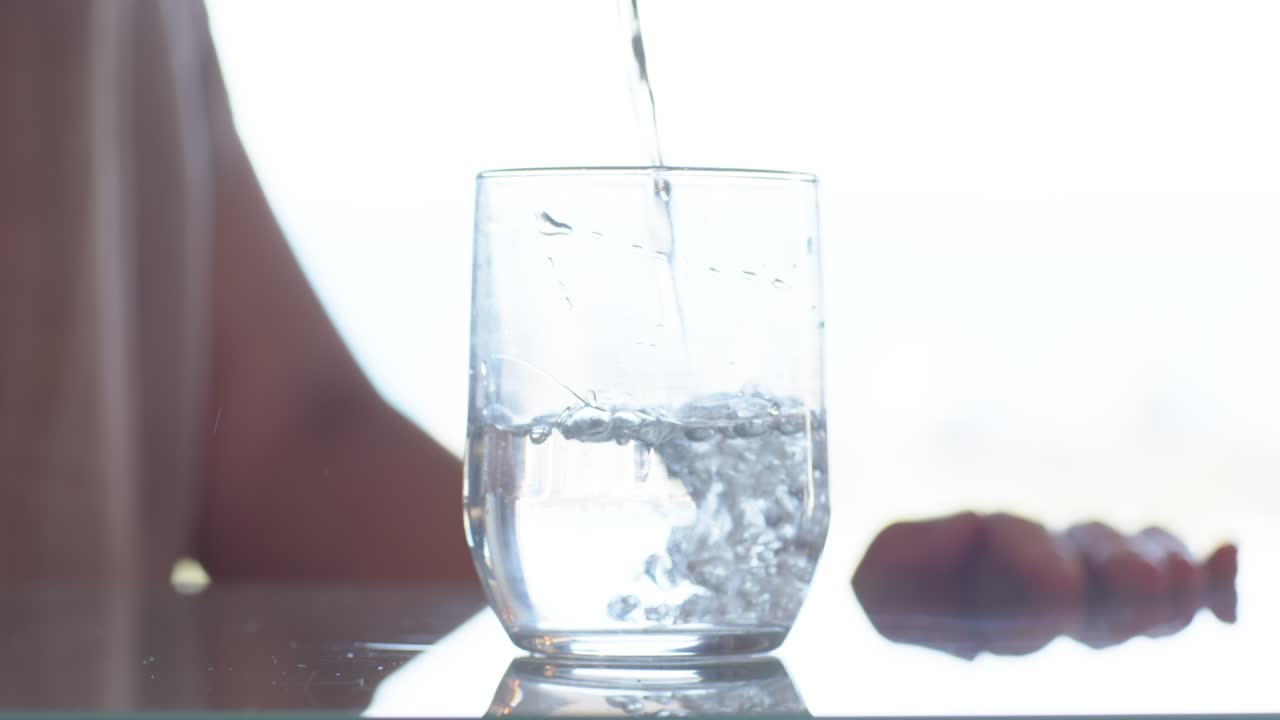 Eine Person gießt links einen dünnen Strahl, dann erhöht der Krug den Fluss in ein klares Glas, das gefüllt wird.