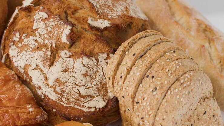 Close-up shot of sourdough loaf, sliced grain bread, and croissants under bright studio lighting.
