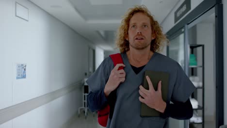 Caucasian-male-doctor-holding-tablet-and-walking-in-corridor,-slow-motion