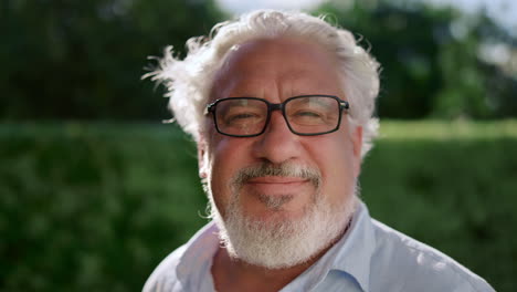 Closeup-senior-man-looking-at-camera.-Mature-man-standing-in-green-park