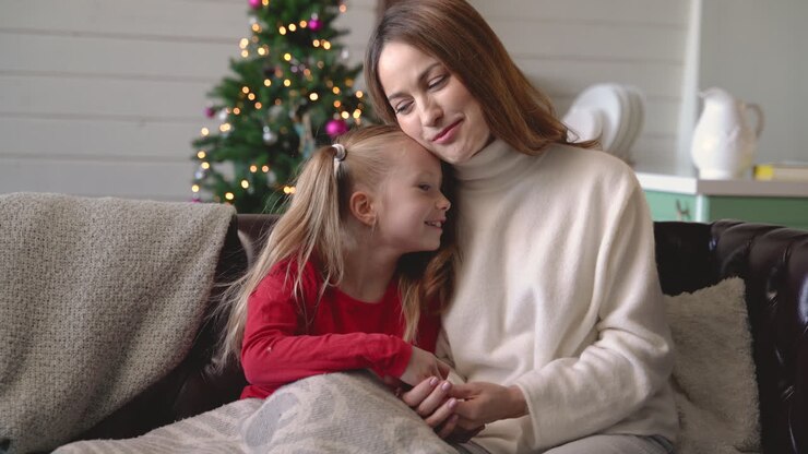 Mutter und Tochter sitzen unter einer Decke auf dem Sofa und unterhalten sich.