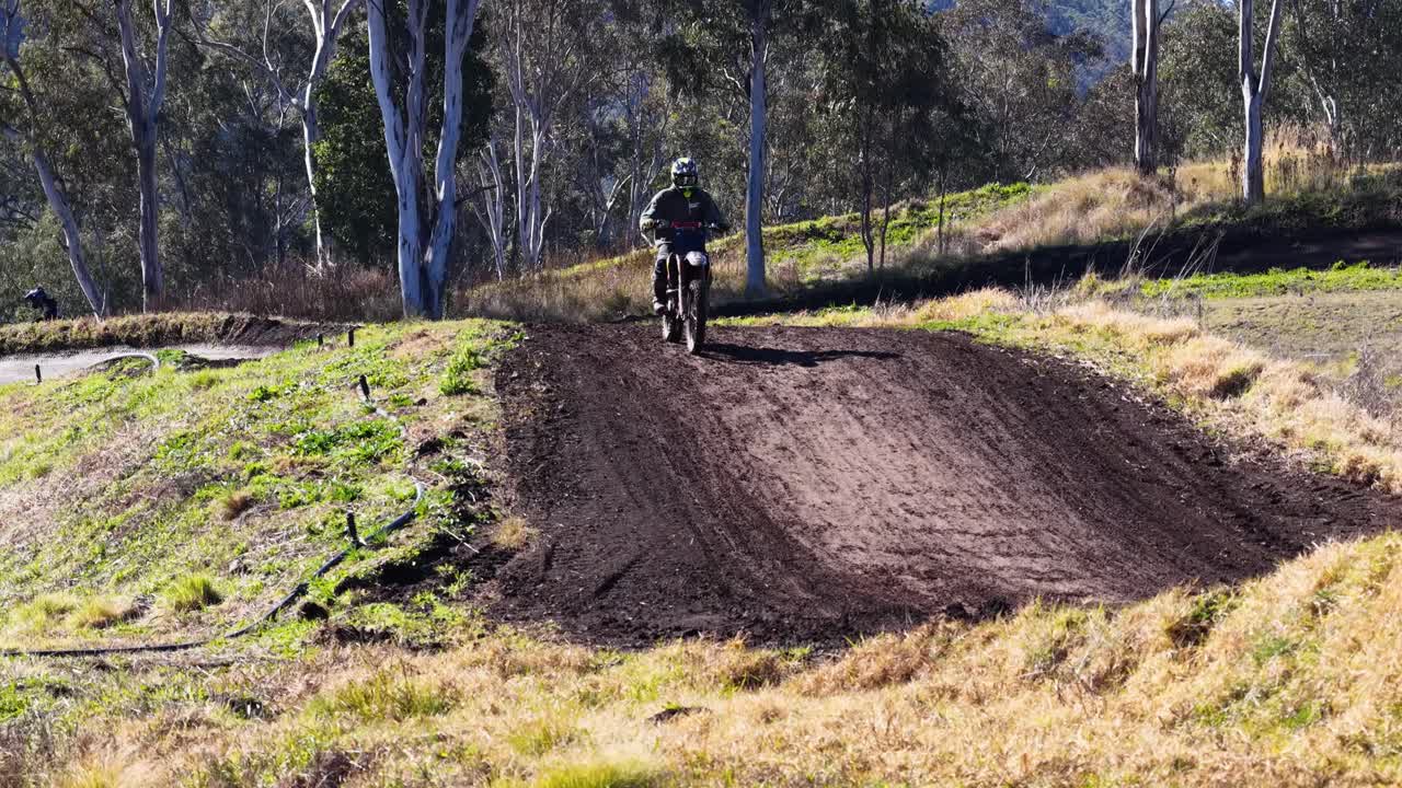 Motocross rider jumps over dirt hill on sunlit outdoor track, camera follows action steadily