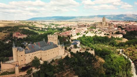 aerial view of the alcázar of segovia and the cathedral of segovia rising above the cityscape and the surrounding landscape on a sunny day with some clouds, drone establishing shot
