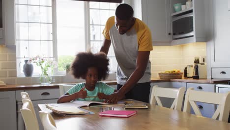 african american daughter and her father doing her schoolwork together at kitchen table