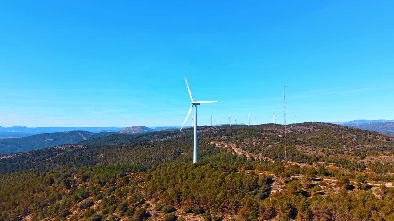 Madrid, Spagna, 8 agosto 2025: Turbina eolica e torre di comunicazione su una cima di montagna boscosa. Veduta aerea di turbina a elica bianca, alto traliccio radio, colline verdi, cielo sereno, telecomunicazioni.