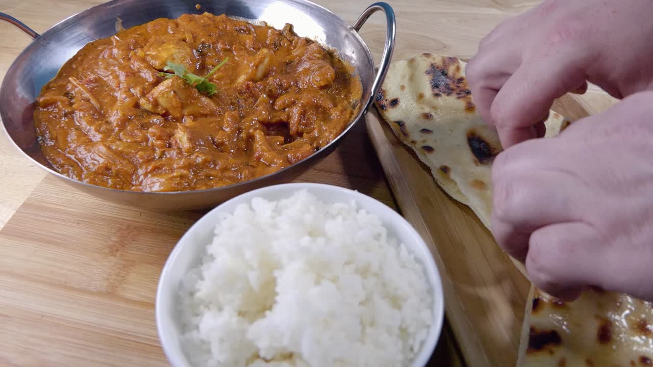 toma deslizante de arrancar un trozo de mantequilla naan y sumergirlo en un curry indio casero en un plato balti con arroz