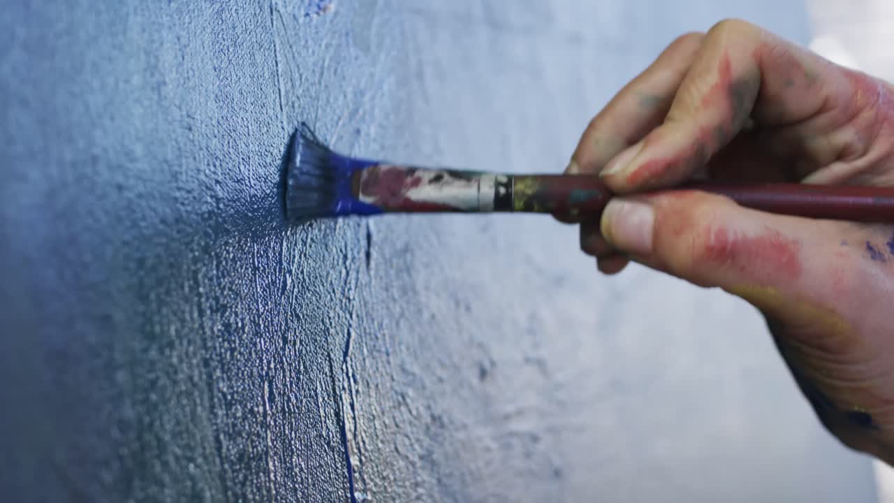 mano de artista femenina biracial pintando en lienzo en un estudio de arte, cámara lenta